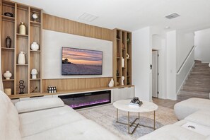 Ein modernes Wohnzimmer mit Kamin, einem an der Wand befestigten Flachbildfernseher und einer Treppe, die in eine weitere Ebene führt.