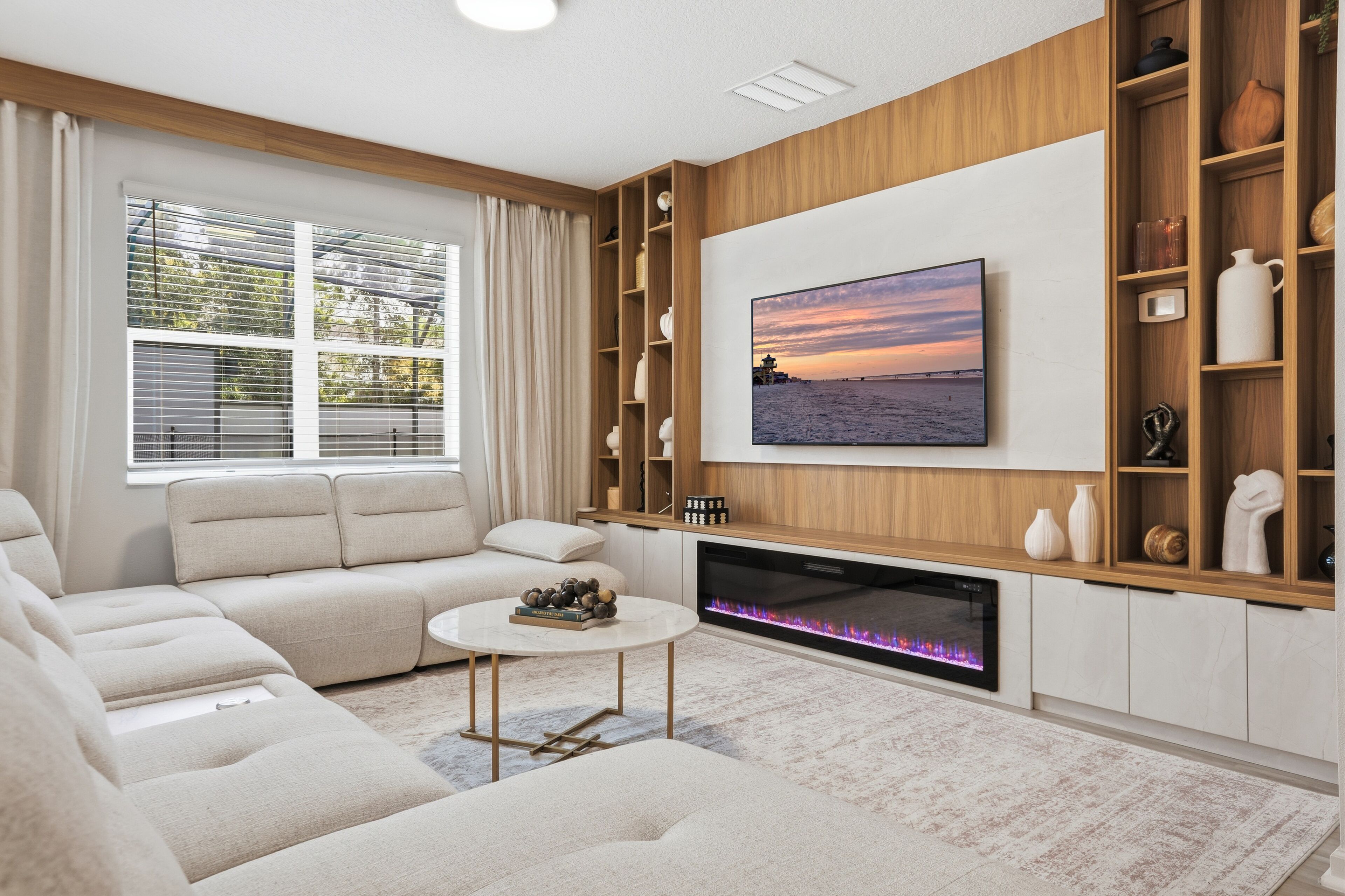 Een moderne woonkamer met een bank, een salontafel, een open haard en een grote televisie aan de muur.