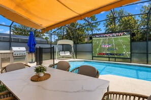 An outdoor pool area with a dining table, chairs, a grill, and a swing chair. - Disney 6BR/4BA Themed Rooms & Pool LED TV BV4509 (Kissimmee)