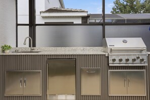 An outdoor kitchen with a built-in grill, a sink, and storage cabinets. - Disney 6BR/4BA Themed Rooms & Pool LED TV BV4509 (Kissimmee)