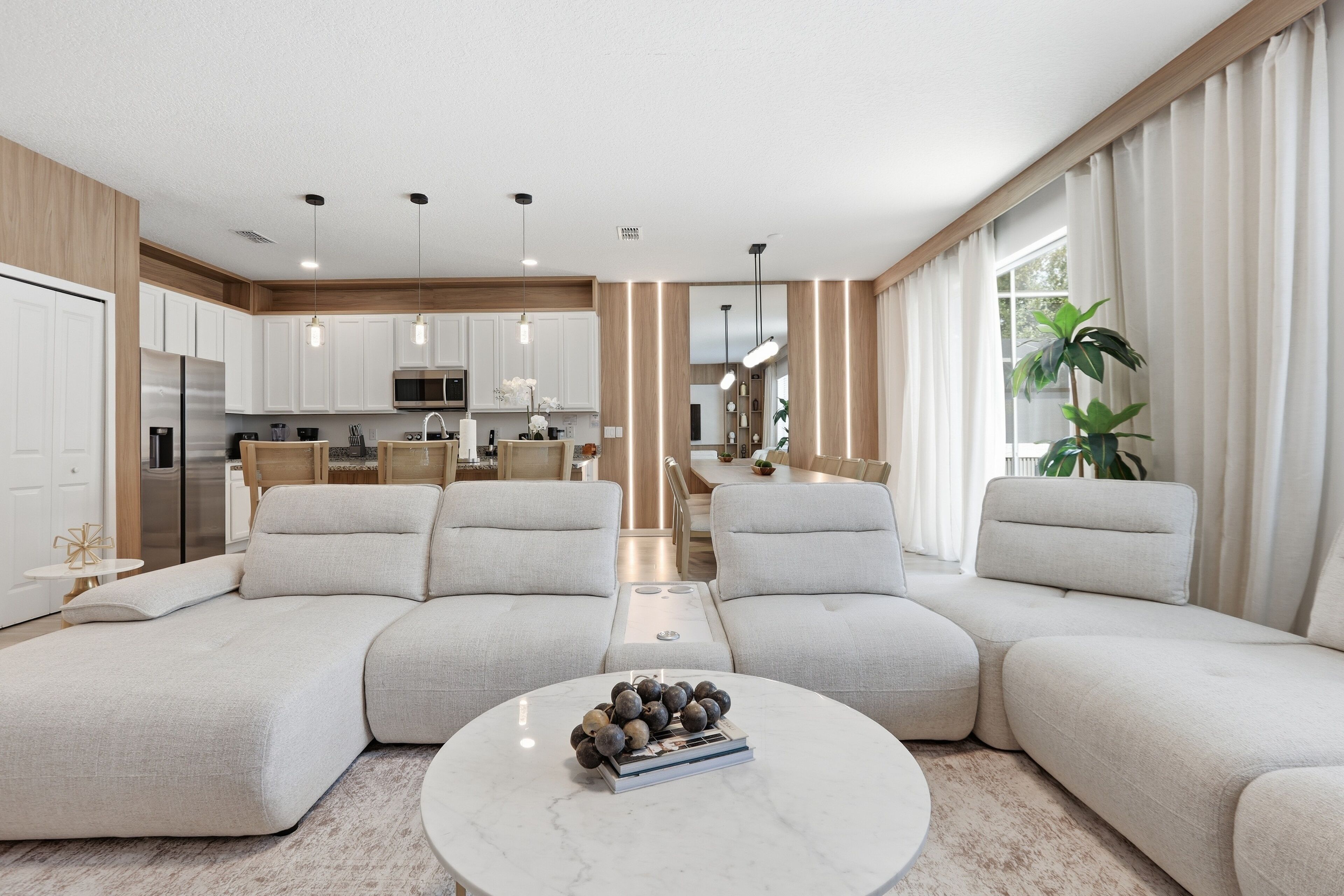 A modern living room with a sectional sofa, a round coffee table with decorative items, and a view into the kitchen area.