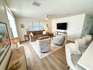 Ein Wohnzimmer mit einer Couch, zwei Sesseln, einem Couchtisch, einem Fernseher und einem Deckenventilator.