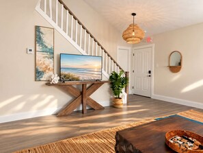 Ein modernes Interieur mit einer Holztreppe, einem Flachbildfernseher auf einem Holzständer, einer Topfpflanze und einem gewebten Korb auf einem Couchtisch aus Holz.