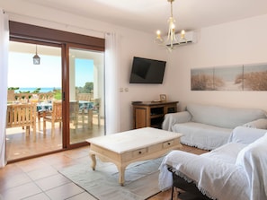 A living room with a sofa, a coffee table, a TV, and a view of the outdoors. - Portichuelo by Interhome (Almuñécar)