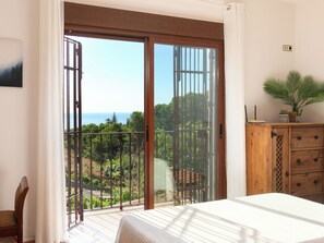 A bedroom with a large sliding glass door leading to a balcony with a view of the sea and greenery. - Portichuelo by Interhome (Almuñécar)