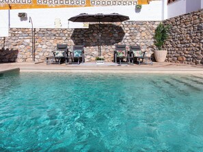 A clear swimming pool with lounge chairs and an umbrella, surrounded by stone walls and a white building. - Portichuelo by Interhome (Almuñécar)