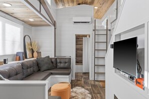 Un interior modern amb un sofà modular, una televisió de pantalla plana i una escala que condueix a una zona d'altell.