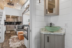 A modern kitchen with white cabinetry, a grey sofa, and a fluffy rug. - Modern Tiny Home | King Bed | A/C | Gas Fireplace (Donnelly)