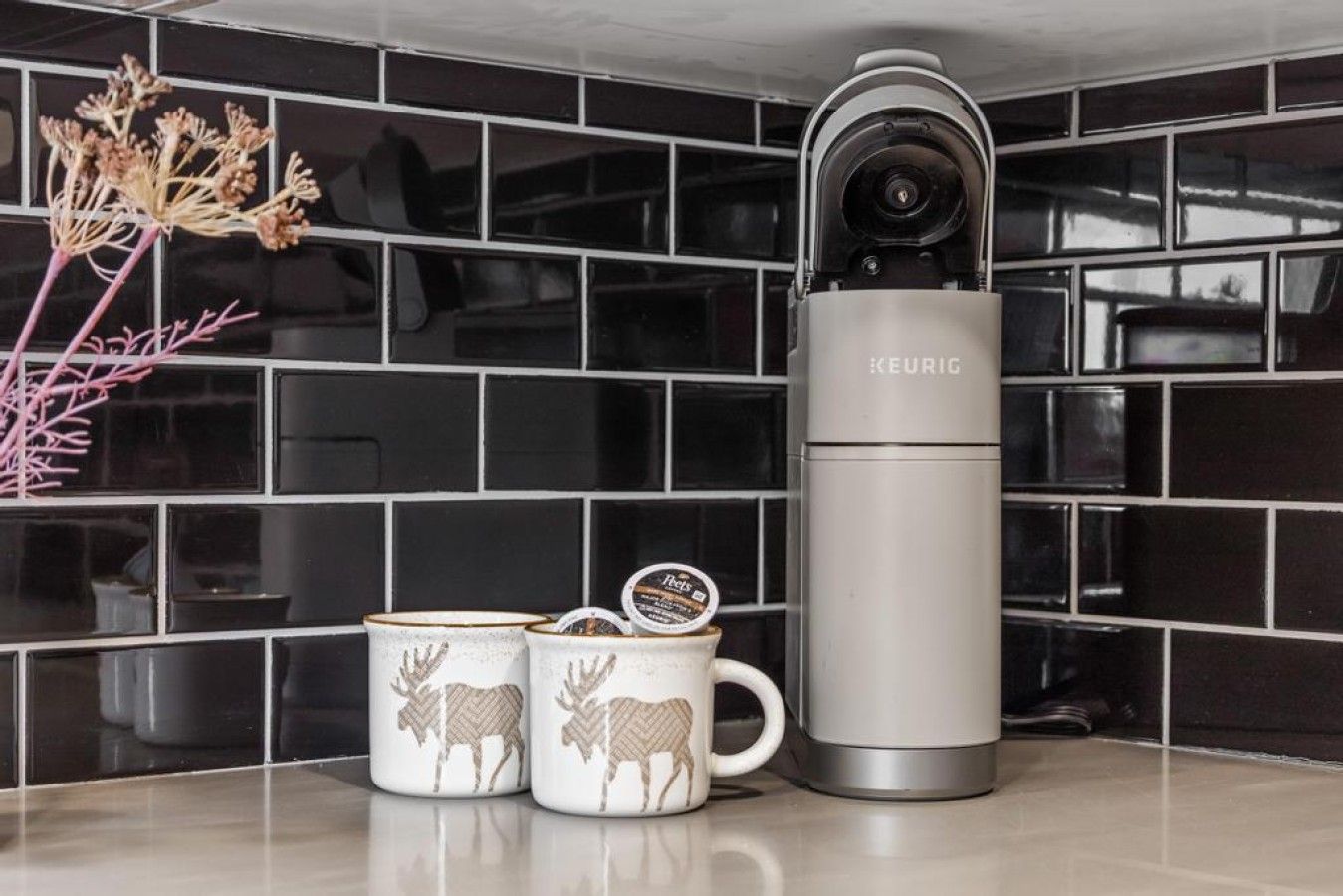 Una cocina con una cafetera KEURIG, dos tazas con diseño de ciervo y una planta decorativa.