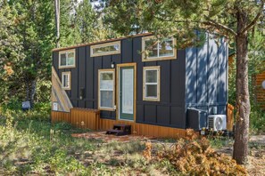 A small cabin with a wooden deck, a door, and a window. - Modern Tiny Home | King Bed | A/C | Gas Fireplace (Donnelly)