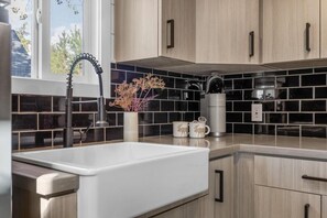 A modern kitchen with a white sink, black backsplash, wooden cabinets, and a window with a view. - Modern Tiny Home | King Bed | A/C | Gas Fireplace (Donnelly)