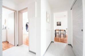 Ein Flur mit Holzboden, weißen Wänden und einer Tür zu einem Raum mit Spiegel und hängender Kleidung.