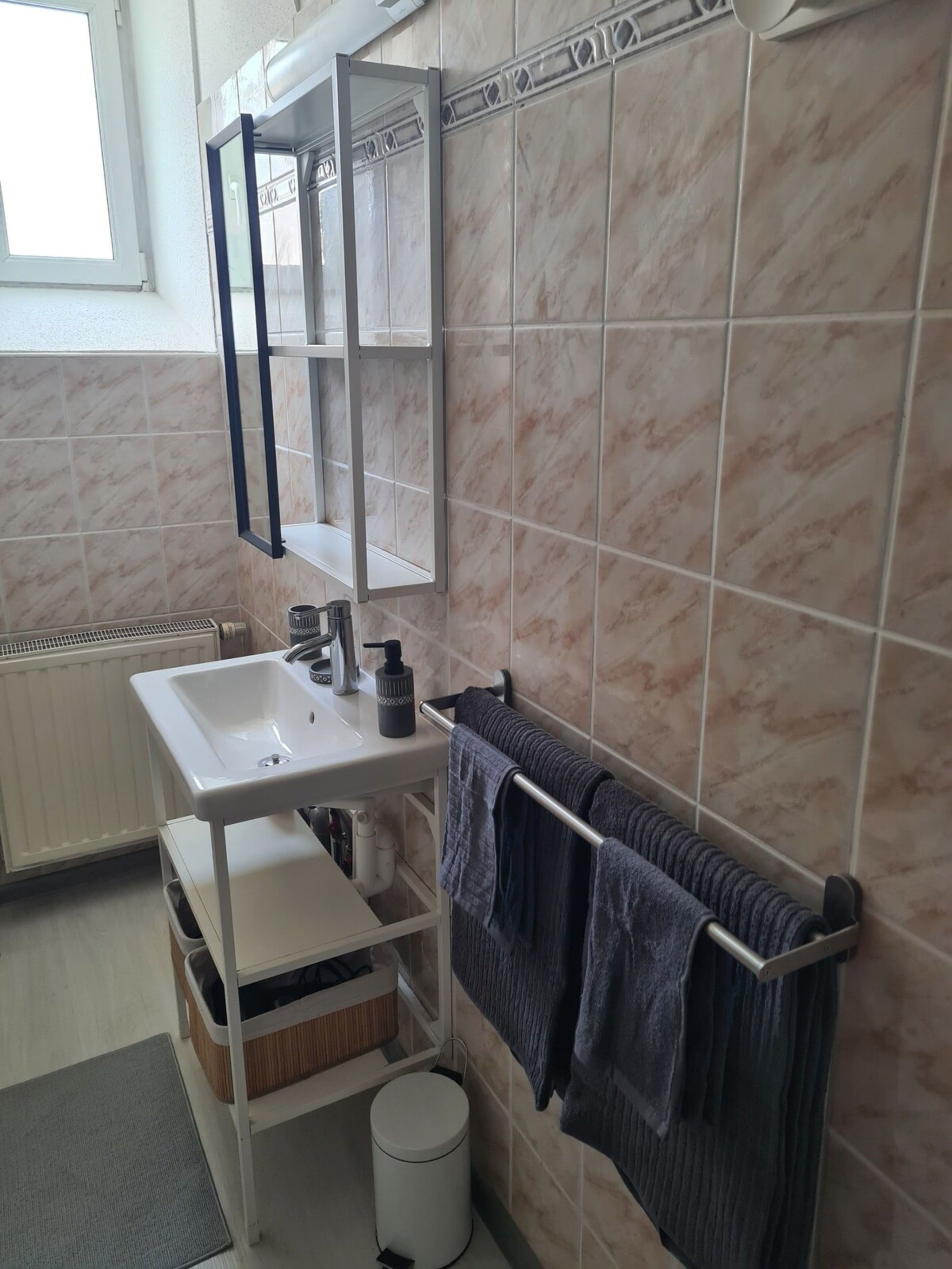 Ein Badezimmer mit einem weißen Waschbecken, einem Handtuchhalter mit Handtüchern, einem Spiegel und einer Heizung.
