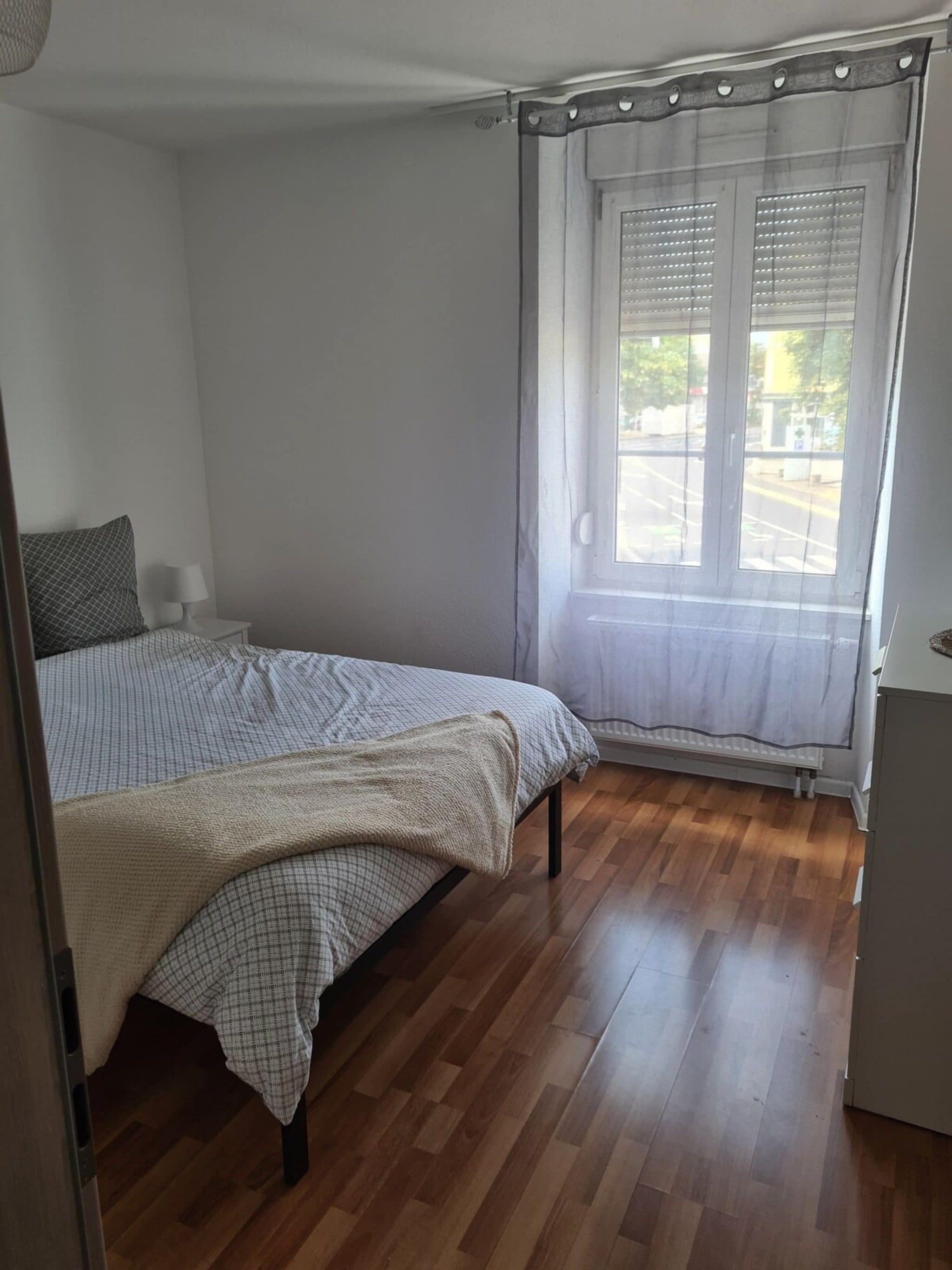 Un dormitorio con cama, una mesita de noche, una ventana con persianas y un radiador.