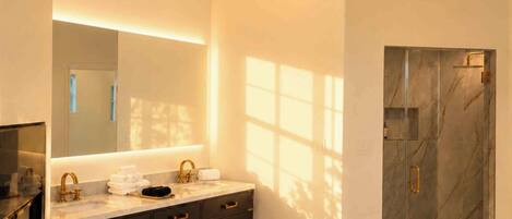 Un baño moderno con ducha de mármol, un espejo grande y un tapete mullido.