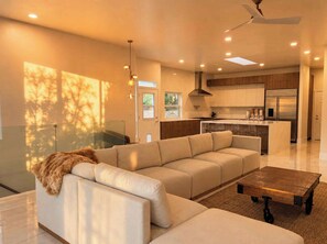 A modern living room with a sectional sofa, a wooden coffee table, and a kitchen in the background. - Luxury Newly Renovated Modern Retreat - Vineyard & Golf Course Views (Escondido)