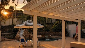 Ett takförsett utomhusområde med en pool, solstolar och en dekorativ vattenfallsanläggning.