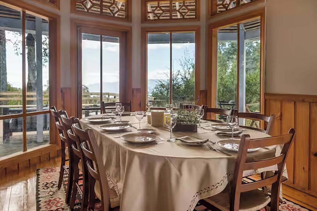 A dining area with a round table set for four, large windows, and a view of the outdoors.