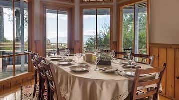 A dining area with a round table set for four, large windows, and a view of the outdoors.