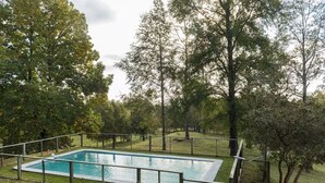 A rectangular swimming pool surrounded by a fence, with trees in the background.