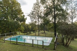 Una piscina rectangular rodeada por una cerca, con árboles al fondo.