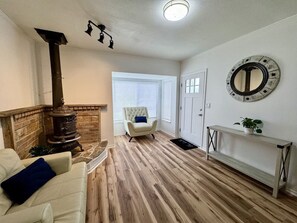 Un salon avec une cheminée, un fauteuil blanc, un banc et un miroir rond accroché au mur.