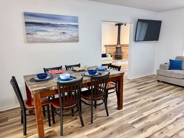 Un coin repas avec une table et des chaises en bois, un tableau accroché au mur et un téléviseur fixé au mur.