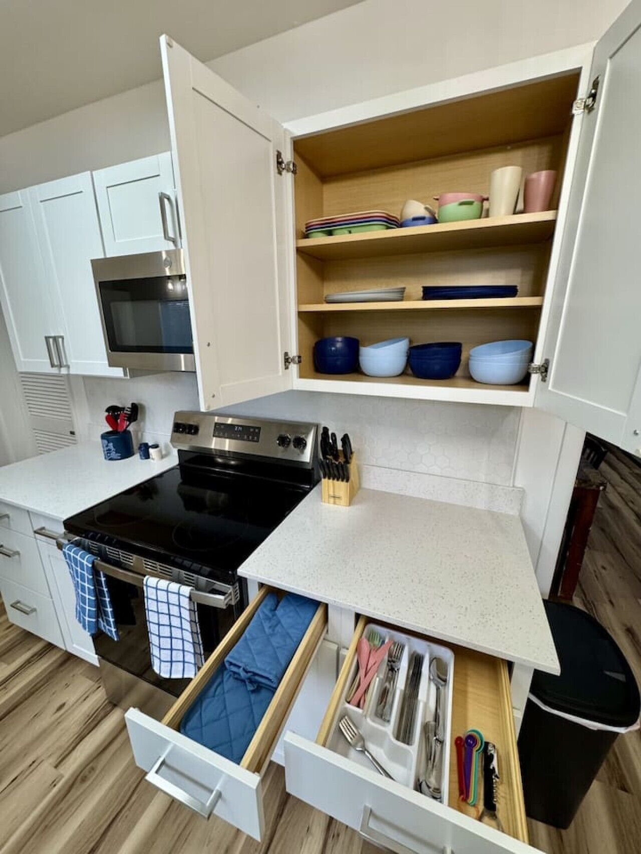 A compact kitchen with a stove, oven, and open cabinets containing dishes and utensils.