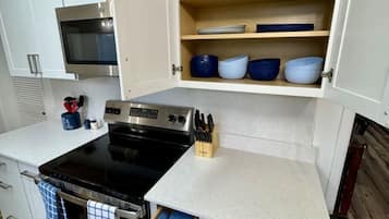 A compact kitchen with a stove, oven, and open cabinets containing dishes and utensils.