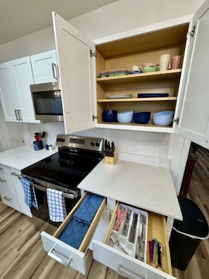 Una cucina compatta con fornello, forno e pensili aperti che contengono stoviglie e utensili.