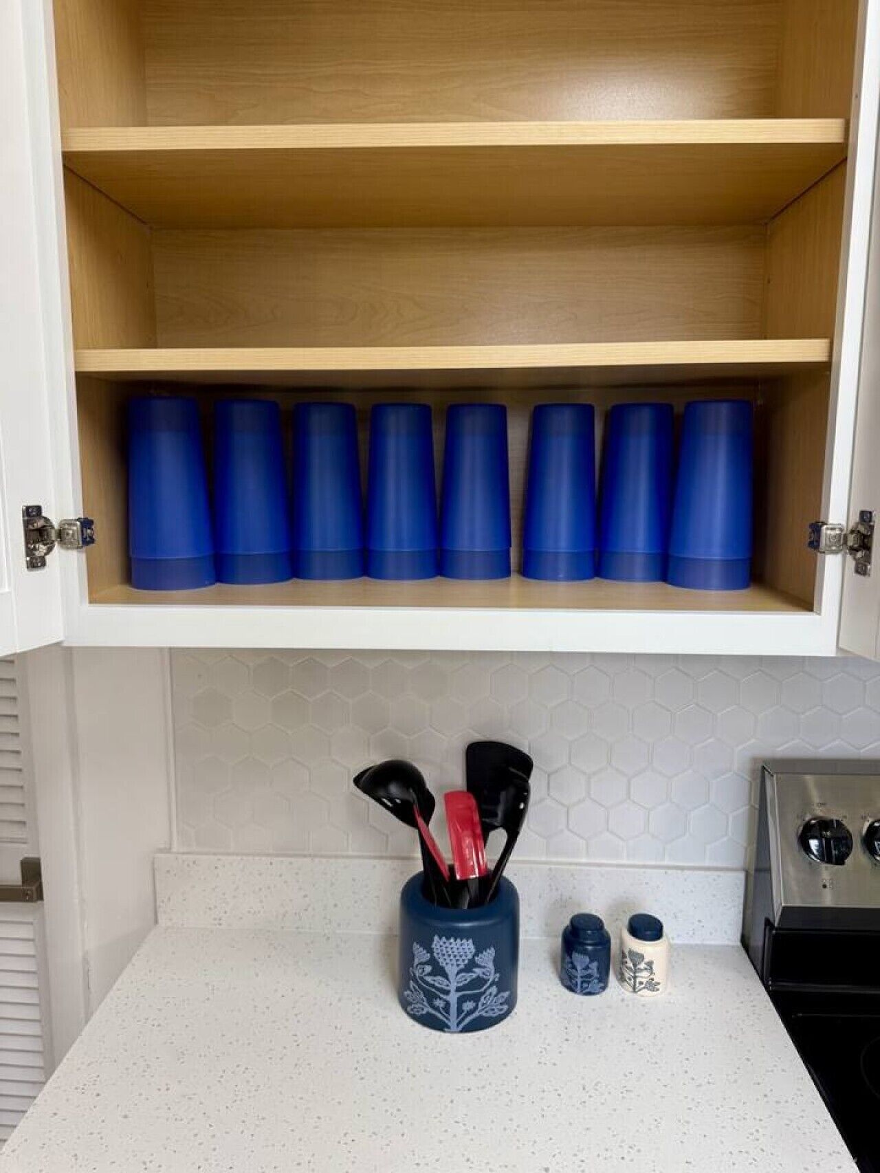 A kitchen with a wooden cabinet above a countertop, containing blue containers and kitchen utensils.