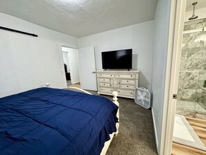 Une chambre à coucher comprenant un lit, une commode, un téléviseur et un espace douche.