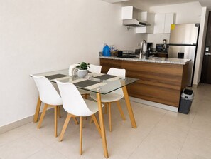 A modern kitchen with a glass dining table, white chairs, and a wooden island.