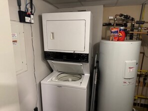 Une buanderie équipée d’un lave-linge et d’un sèche-linge à chargement frontal, d’un chauffe-eau et de tuyauteries apparentes.