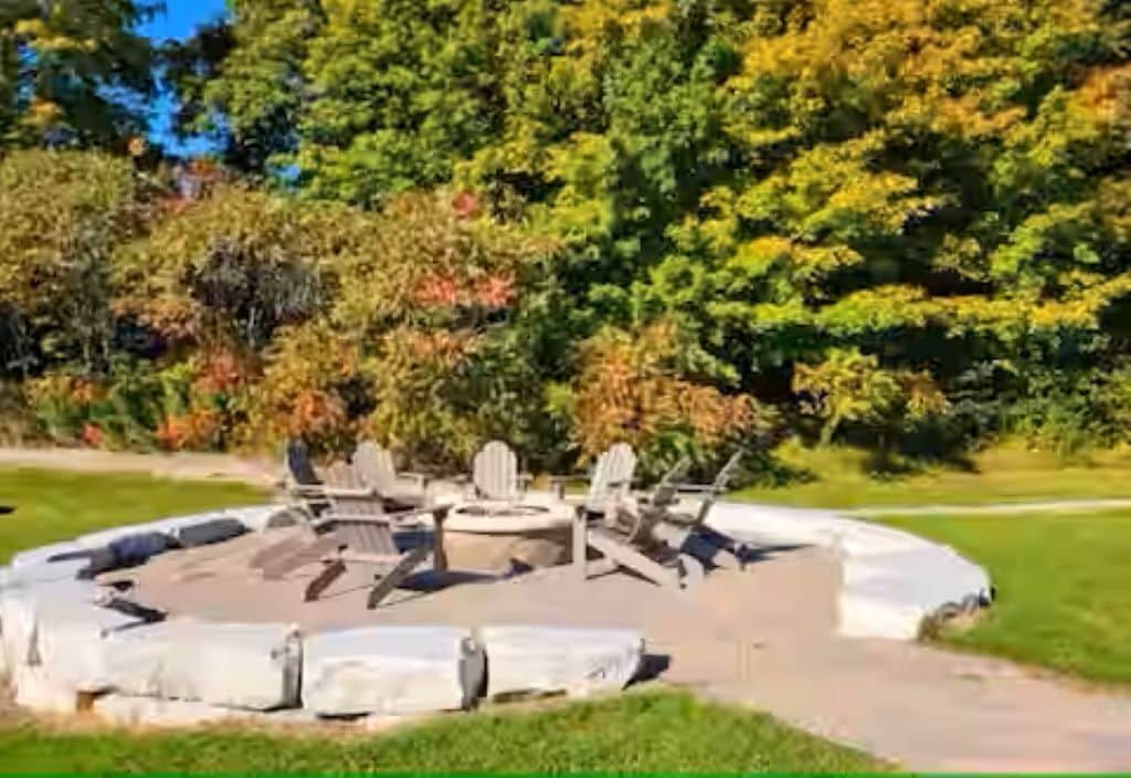 A circular outdoor seating area with Adirondack chairs and a fire pit.