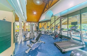 Uma academia com diversos equipamentos de exercício, janelas amplas e teto de madeira.