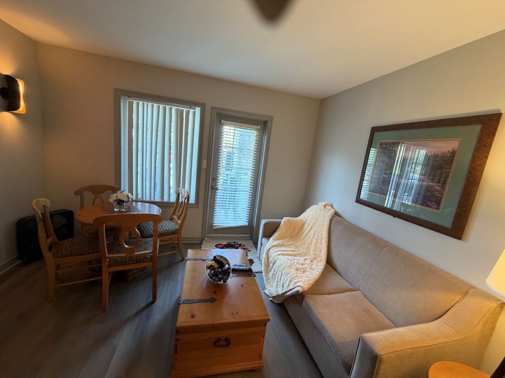 Ein Wohnzimmer mit einer Couch, einem Couchtisch, einem Esstisch mit Stühlen und einem gerahmten Bild an der Wand.