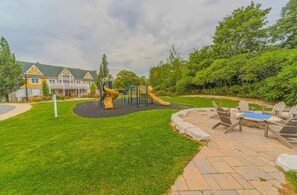 Une aire de jeux dotée d’un toboggan et d’éléments d’escalade, entourée d’une pelouse bien entretenue et d’un espace patio aménagé avec du mobilier d’extérieur.