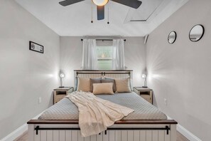 A bedroom with a bed, bedside lamps, a ceiling fan, and a window with curtains. - Family & Sports Team Oasis Near Legoland & Parks (Winter Haven)