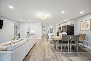 A modern kitchen with white cabinetry, a dining area with wooden tables and chairs, and a built-in seating area with a white sofa. - Family & Sports Team Oasis Near Legoland & Parks (Winter Haven)