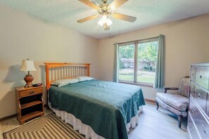 Ein Schlafzimmer mit Bett, Nachttisch, Schminktisch, Stuhl, Fenster und Deckenventilator.
