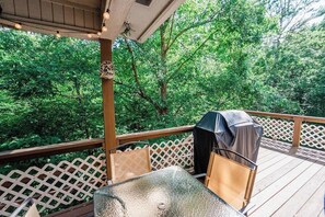 Eine überdachte Terrasse im Freien mit Tisch und Stühlen, umgeben von einem Holzzaun und Bäumen.