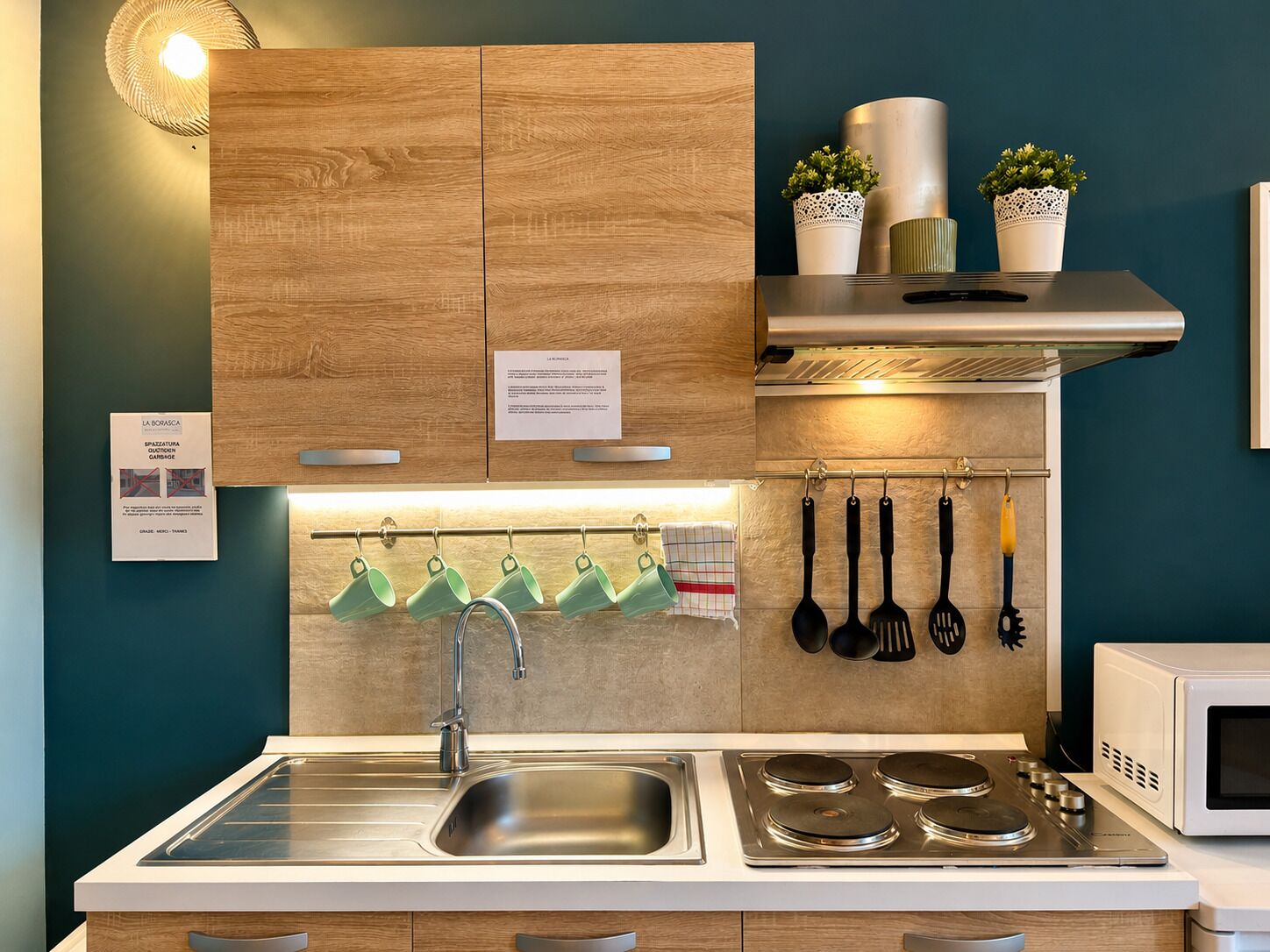 Een moderne keuken met houten kastjes, een RVS-gootsteen, een fornuis en hangend keukengerei.