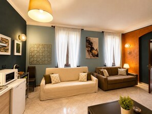 Ein Wohnzimmer mit zwei Sofas, einem Couchtisch, einem Fernseher, einer Mikrowelle und einer kleinen Küchenzeile.