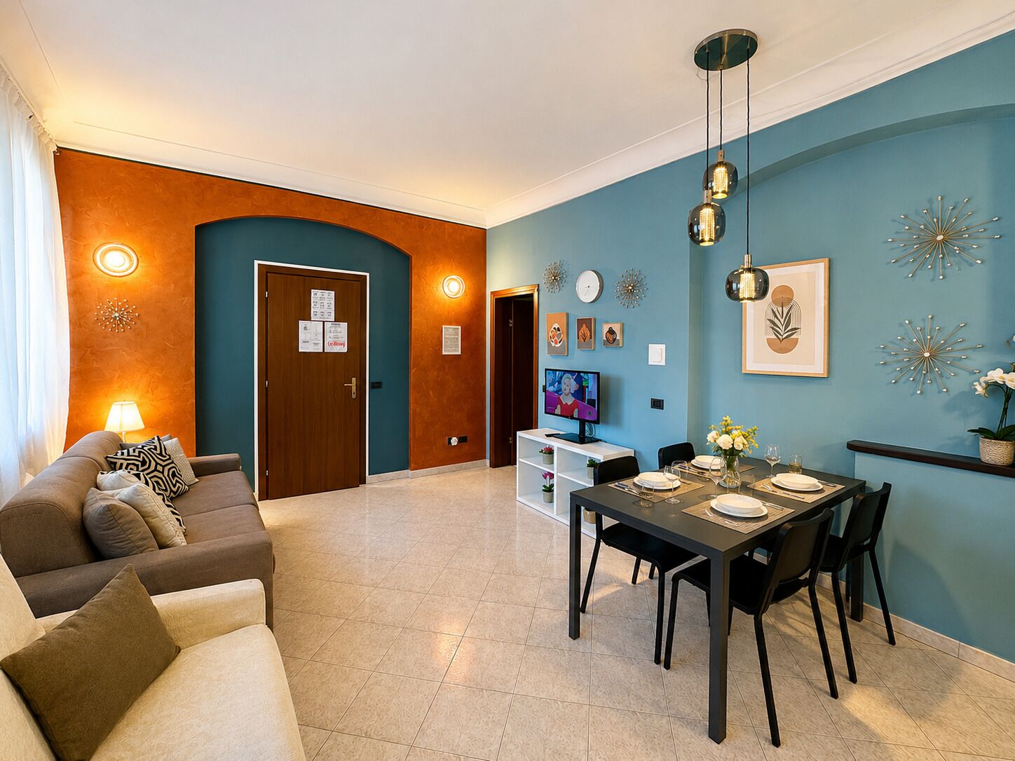 Een moderne woonkamer met een bank, een eettafel voor vier personen en een televisie op de achtergrond.