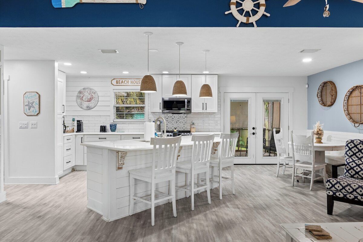 A modern kitchen with white cabinetry, a central island with bar stools, pendant lighting, and a view to the dining area.