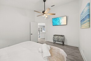 A bedroom with a bed, a ceiling fan, a painting, and a view into another room. - 3BR Charming PCB House, Fire Pit, Fenced Yard (Panama City)
