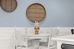 A white wooden bench with a round table in front, a wall-mounted woven basket, and a wall-mounted mirror. - 3BR Charming PCB House, Fire Pit, Fenced Yard (Panama City)