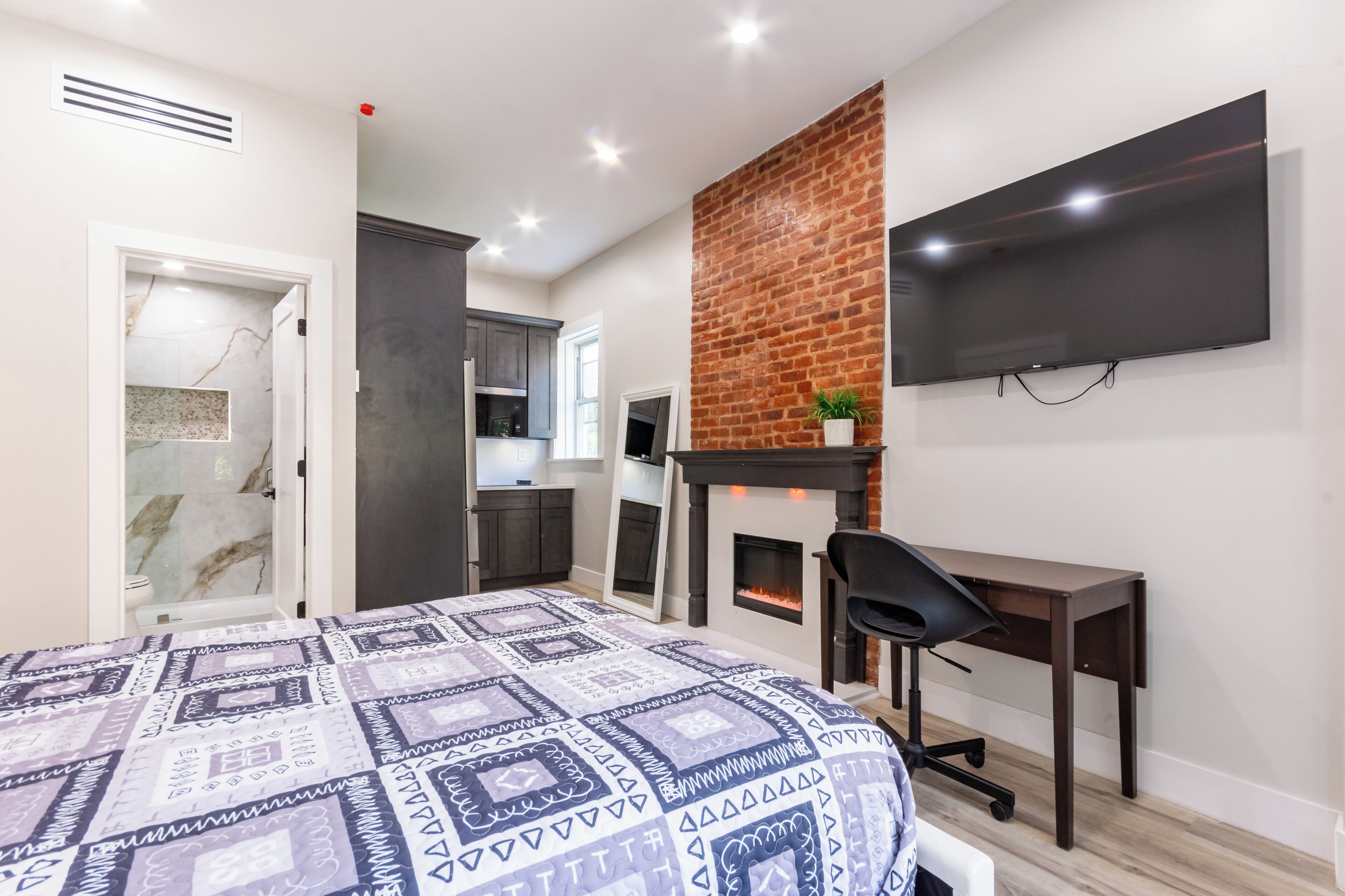 Ein Schlafzimmer mit Bett, Schreibtisch, Fernseher, Kamin und eigenem Bad.