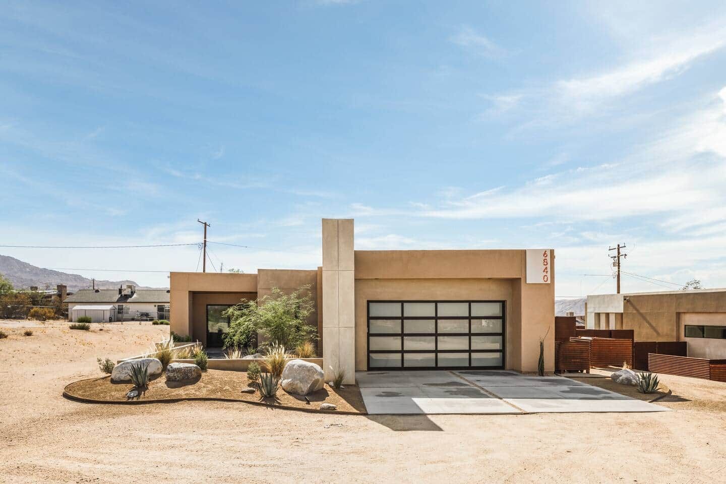 Une maison moderne de plain-pied avec un garage, entourée d’un aménagement paysager de style désertique.